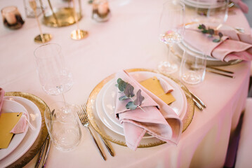 Wedding banquet. The festive table is served with plates with napkins and name cards, glasses and cutlery, and decorated with flower arrangements and candles