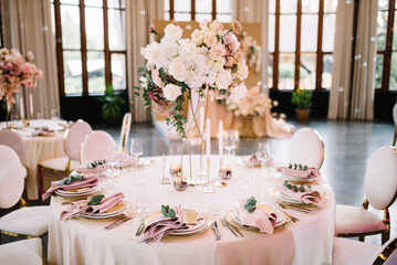 Wedding banquet. The festive table is served with plates with napkins and name cards, glasses and cutlery, and decorated with flower arrangements and candles
