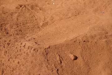 Rot-braune Sandfläche mit Spurenmuster bei Sonne im Frühling