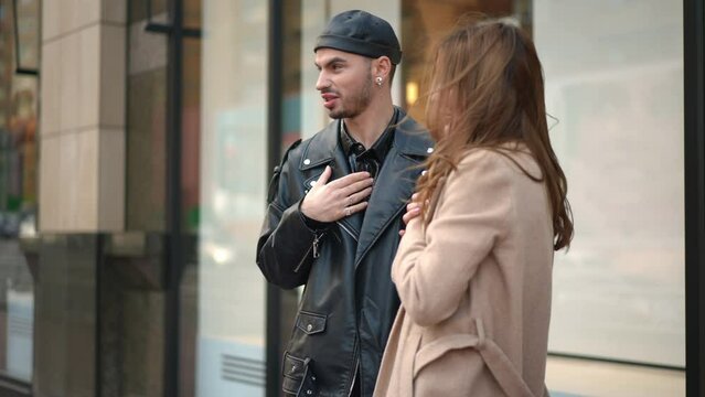 Side view stylish Caucasian gay man and young woman standing on city street mocking discussing people outfit. Arrogant young millennial friends sneering gossiping outdoors in urban city
