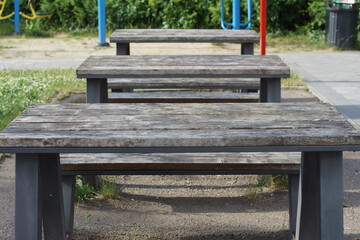 Naklejka premium three wooden tables with benches stand on the ground during the day in a recreation area in a park in summer