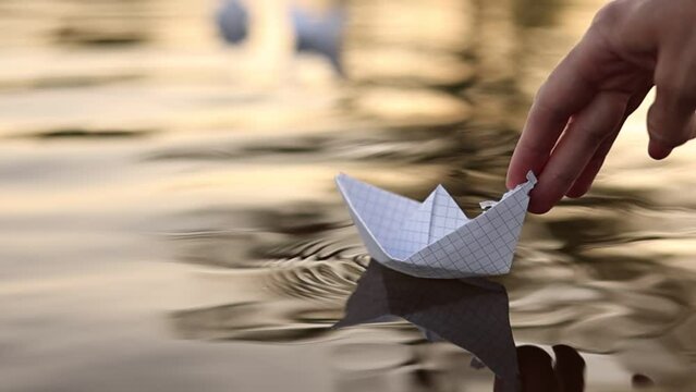 child puts a paper boat into the water. happy family fantasy kid dream concept. child playing with paper boat ship. a child hand launches a boat in a park in a lifestyle pond