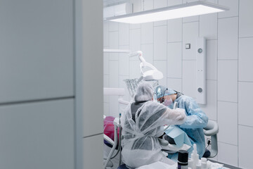 The process of preparing and cleaning teeth. A female professional dentist and an assistant are working. Photo through the door