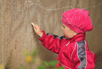 Child 3 years old, Caucasian girl, draws with chalk on the wall. Place to copy.