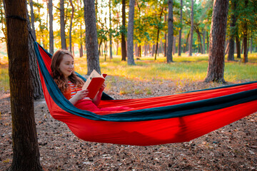 Smiling woman reading a book, relaxing on the hammock in forest, leisure time and summer holiday concept