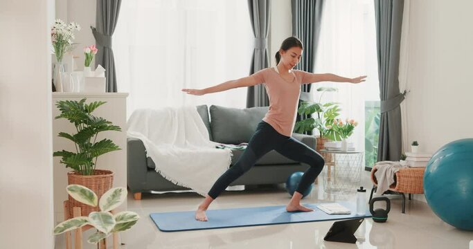 Young attractive Asia woman in sportswear watching fitness online video on tablet practice yoga for beginner in living room at house.