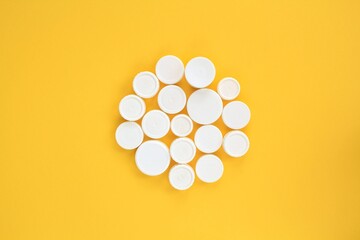 Circle mosaic decoration made of used white plastic bottle caps on yellow background. Handmade craft. Recycling diy art. Nature pollution concept. Garbage design idea. Reuse, reduce flatlay, top view