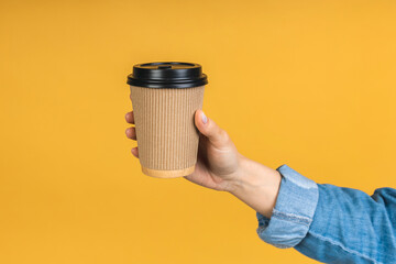 Have a break! Close-up photo of woman's hand holding paper cup of coffee take away, isolated over yellow background. - 512674594