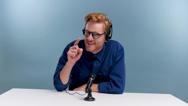 Man recording podcast in blue studio. Male with headphones doing vlogging radio host broadcasting with professional microphone.