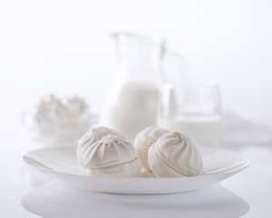 White airy marshmallows in a white dish against a background of glassware with milk on a white...