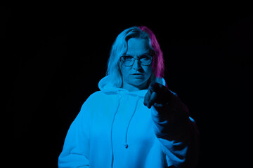 woman with glasses in a hoodie points her finger at you in blue light on a black background