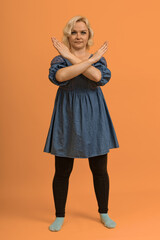 plus size blond woman in blue dress showing stop with crossed arms on color background