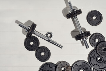 Fitness or bodybuilding concept on white wooden flooor background. Sport equipment for training at home. Photograph taken from above, top view with lots of copy space