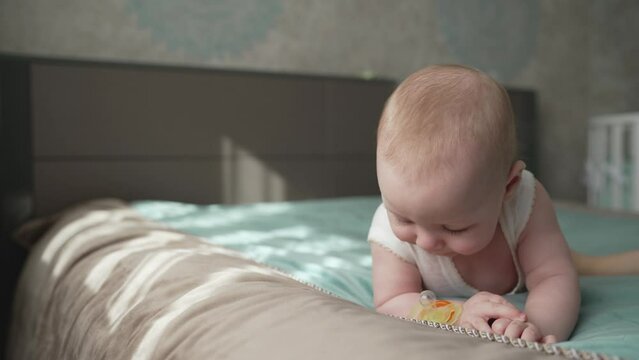 A little boy's nipple falls out of his mouth. A contented boy with a pacifier in his mouth is lying on the bed. A little boy lies on the bed and spits a pacifier out of his mouth.