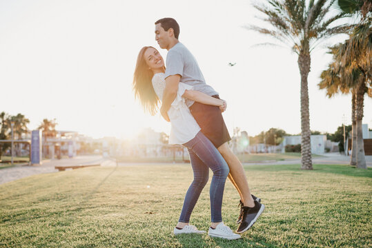 A full-length photo of a happy brunette girl who is lifting her Hispanic boyfriend