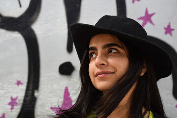 Closeup portrait of young girl in fedora hat with graffiti wall behind