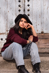 Portrait of young stylish woman in fedora hat sitting on steps of old building