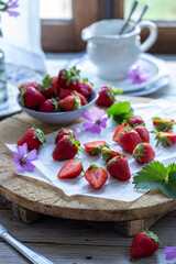 Fragole sparse tagliate a metà o intere insieme a foglie di fragola e fiori di malva