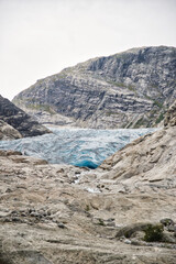 The end of the Jostedalsbreen glacier in Norway shows amazing blue-colored ice forming a small cave in the middle of a rocky landscape. Aventure, hiking, and trekking background. Travel destination.  