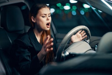 Fototapeta na wymiar horizontal photo of a woman sitting at the wheel of a car and screaming loudly with her eyes closed holding the steering wheel from fright