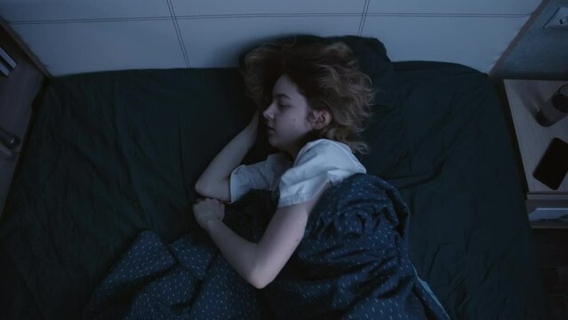 A young woman lies in bed and tries to sleep at night. She rolls from side to back and back, then back to back. She is a little annoyed. Slow motion 4k footage