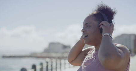 Plus size woman tracking her goals on her smartwatch and running in city. Larger active african american woman getting fit with a routine outdoor workout. Listening to music playlist in headphones