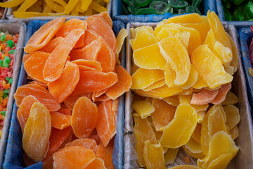 Candied fruits, mango pieces in yellow and orange colors. A pile of candied slices in boxes at the market.