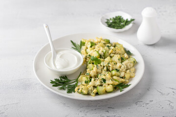 Turkish scrambled eggs with zucchini served with yogurt on a light blue background. Delicious homemade vegetarian food