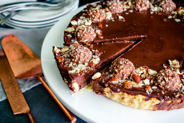 Closeup View of Sliced Chocolate Hazelnut Tart: Chocolate ganache tart garnished with candy and chopped nuts