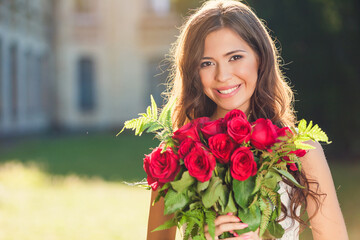 Young brunette woman outdoors in the park with a bouquet of red roses