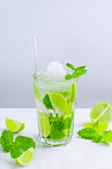 Mojito cocktail on a light background. Summer cool frappe cocktail with lime and mint. Cool refreshing drink served with mint and green citrus fruit.