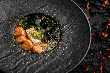 Asian miso soup ,soy sauce, greens and baked salmon. On a black stone background, macro