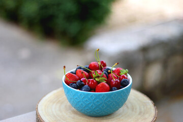 Bowl filled with strawberries, blueberries and cherries in the garden. Selective focus.