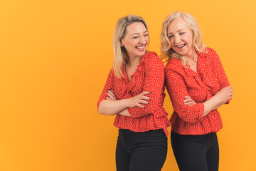 Medium studio shot on yellow or orange background of two adult caucasian female friends standing...
