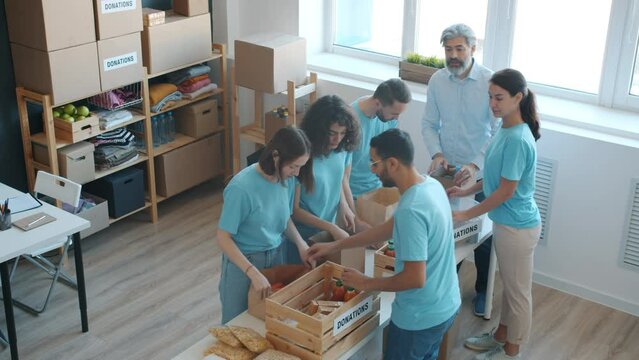 Group of students in uniform packing food for charity and talking to manager in office. Humanitarian aid and provision for poor concept.