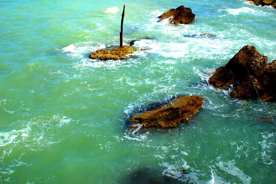 Detail from the Trabocchi Coast on the Adriatic Sea with foaming green waters skimming some rough brown rocks on a gorgeous summer day