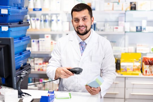 Portrait of positive male pharmacist scanning product while working at cash desk in drug store