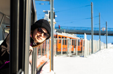 Obraz premium Happy woman in sunglasses sticking head out of window of mountain express train passing among snowy areas on sunny winter day 