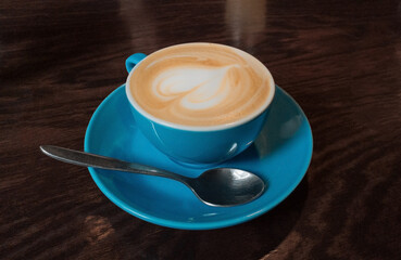 Cappuccino. Close up photo. Cream coffee in bright blue cup on wooden table