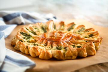 Delicious pie with spinach and ricotta cheese in the shape of a sunflower, towel next to it, close-up.