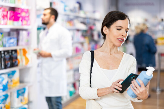 Woman photographing skin or hair care product with smartphone while standing in drugstore.