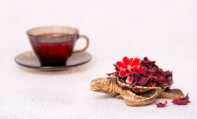 Flower tea karkade. Delicious herbal tropical drink on a bright table. A cup of pink tea from dry hibiscus petals, a natural medicinal drink against the background of fern leaves. Tropical morning.