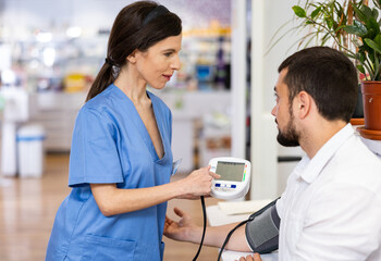 Nurce measuring man's blood pressure in drugstore. Diagnostic procedure in pharmacy.