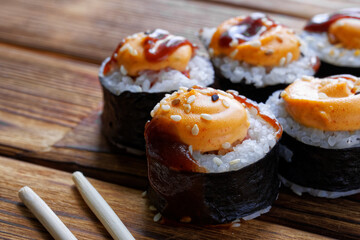 Appetizing rolls with rice, nori, fish and spices and sticks - varibashi on a table made of natural pine boards. Macro. Selective focus.