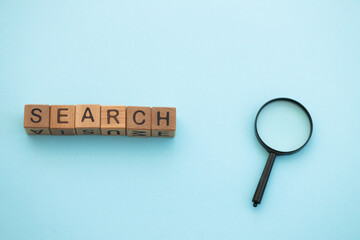 Magnifying glass and word search written wooden cubes on blue background. Search concept