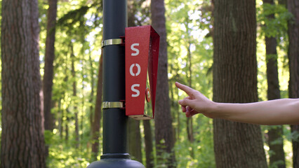 girl's hand press SOS button in park. Red intercom in park for emergency communication, woman's...
