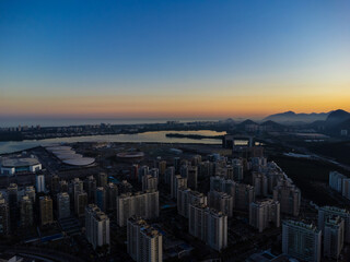 Fototapeta premium Aerial view of Jacarépagua lagoon in Rio de Janeiro, Brazil. Residential buildings and mountains around the lake. Barra da Tijuca beach in the background. Sunny day. Sunset. Drone photo