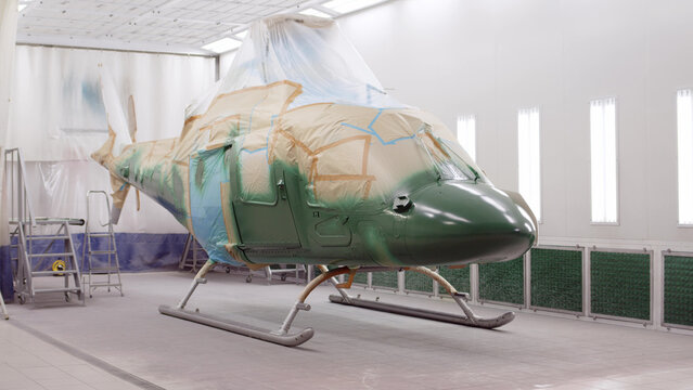 Military Or Civilian Helicopter Stands In Spray Booth And Is Painted Khaki Green. Aircraft Is Being Repaired At Docks. Business Helicopter Painted And Recolored. Military Equipment For Maintenance.