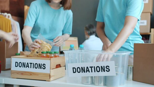 Team of activists men and women packing food in donation boxes working in charity fund helping needy people. Humanitarian aid and provision concept.