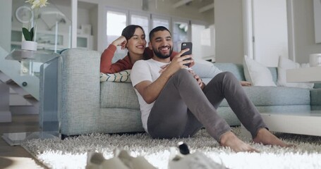 Happy and affectionate mixed race couple using a phone to text message, online chat or browse social media. In love boyfriend and girlfriend laughing while relaxing together on the sofa at home - Powered by Adobe
